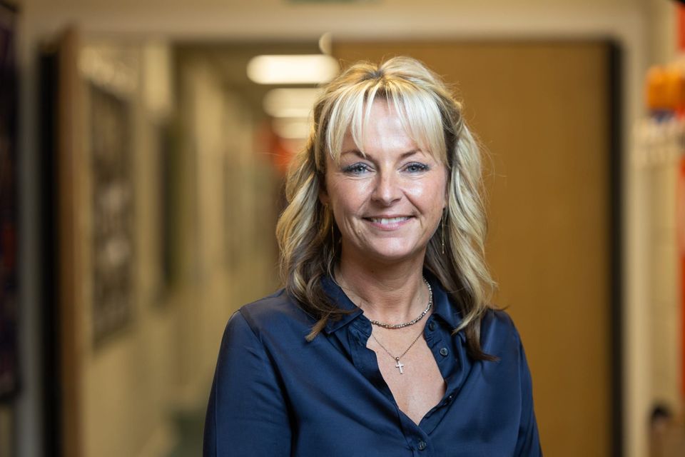 A smiling woman named Jo Campbell with blonde hair stands in a hallway.